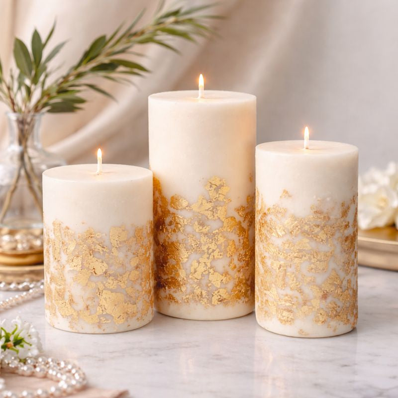 Lit scented pillar candles with gold decoration arranged in a soft neutral home interior