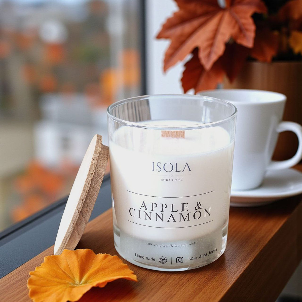 Apple and cinnamon soy wax candle with wooden lid beside a coffee cup in a cosy autumn setting