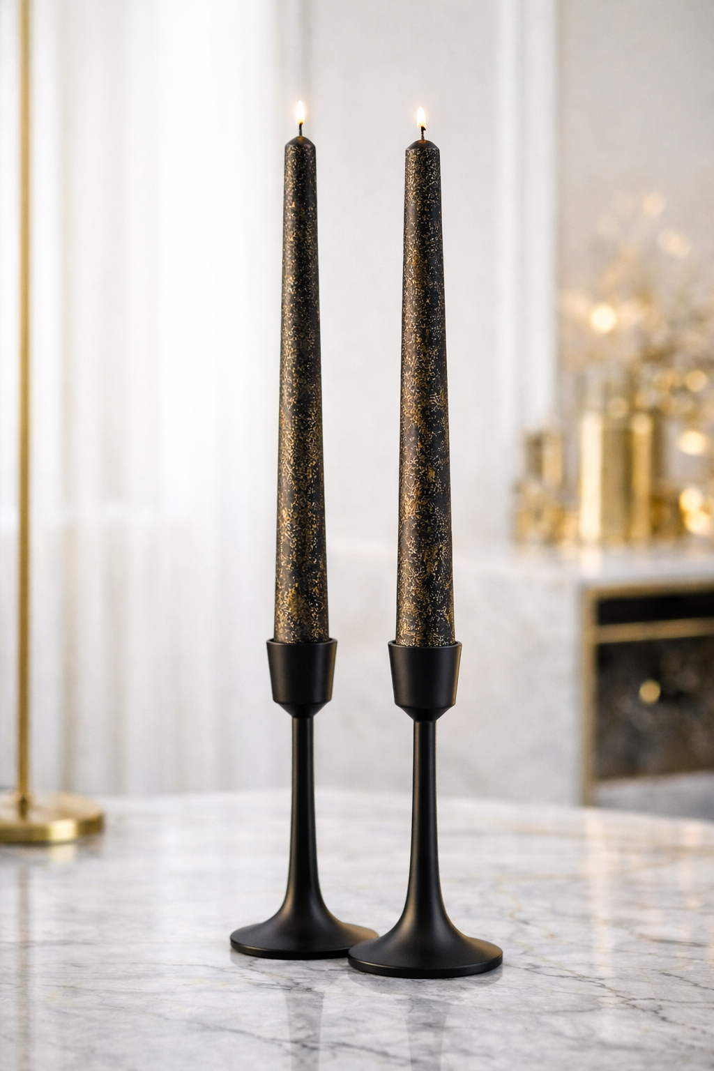 Two black and gold taper candles burning in black candle holders on a marble table