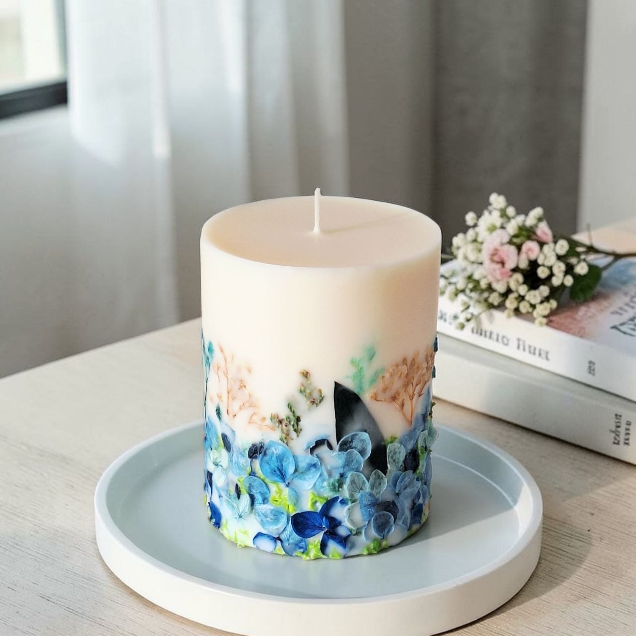Blue botanical soy wax candle displayed on a tray with soft floral home decor