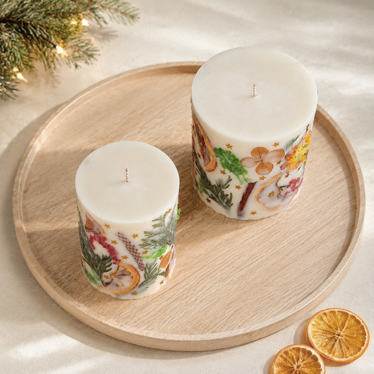 Top view of two Christmas pillar candles on a wooden tray with evergreen and dried orange slices.