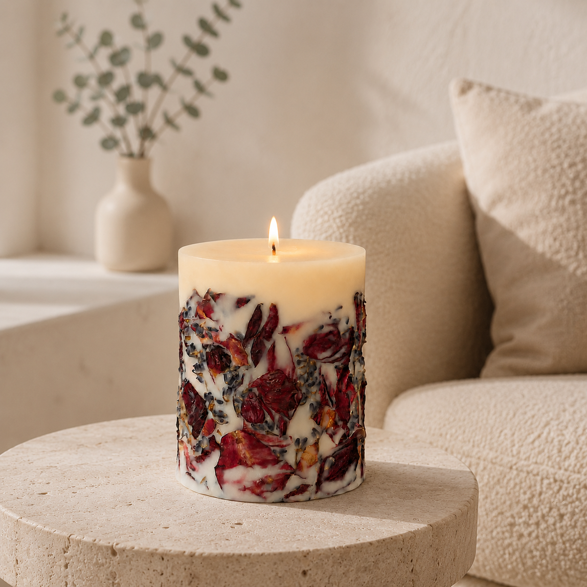 Botanical candle burning on a pale stone table in a softly lit cream living room with a boucle armchair and ceramic vase in the background.
