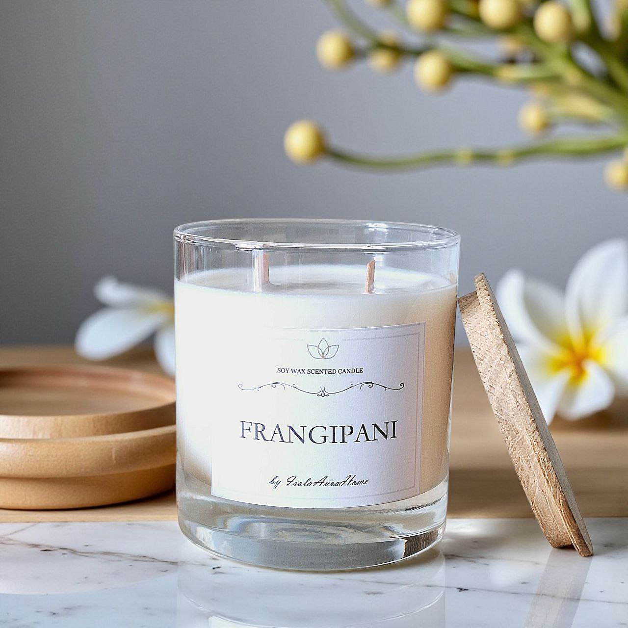 Frangipani soy wax candle in a glass jar with wooden lid, shown open with tropical floral decor