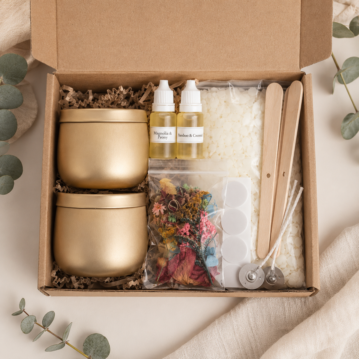 Open gift box with two gold tins, soy wax, fragrance oils, cotton wicks and candle making tools for a DIY candle kit