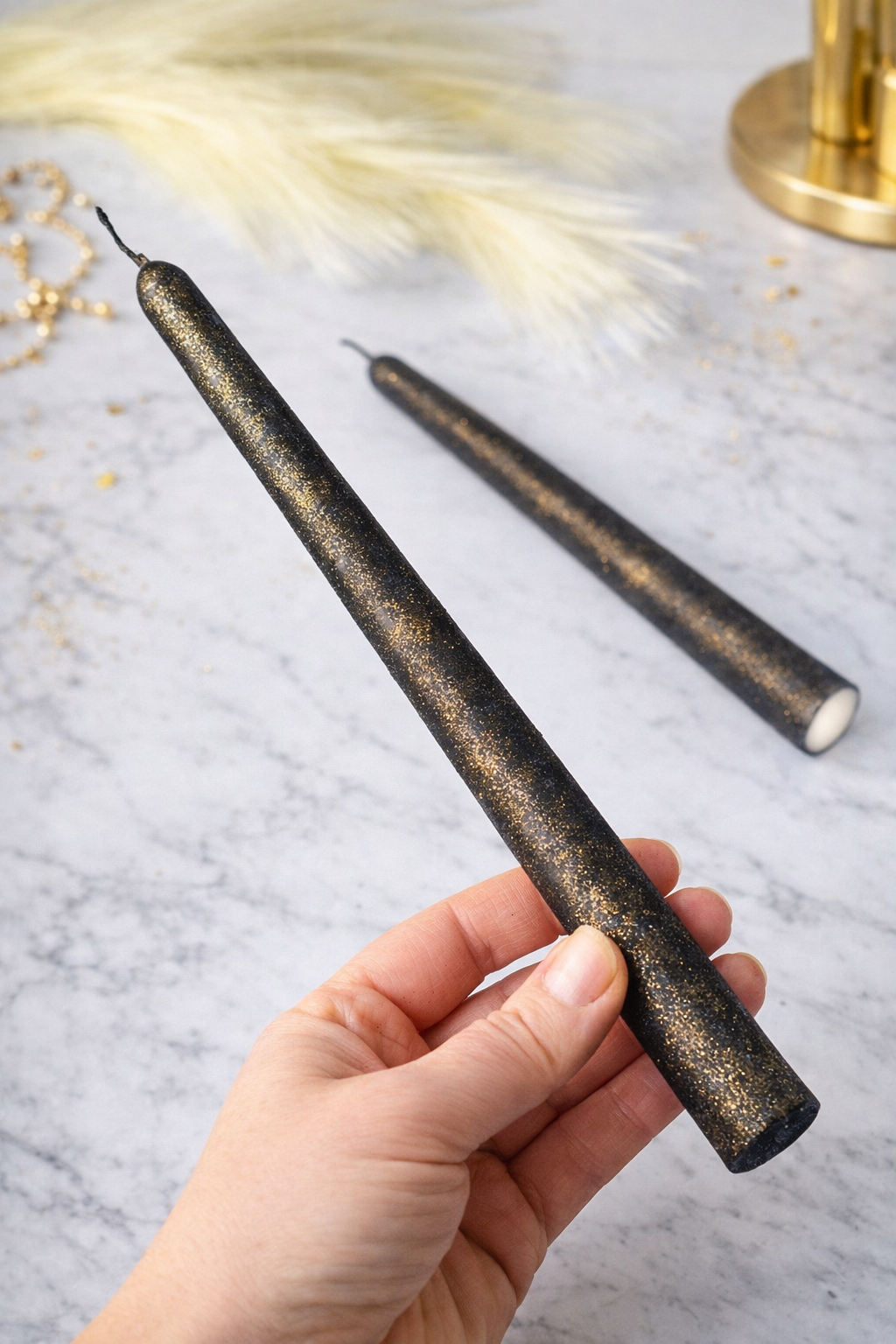Hand holding a slim handmade black soy wax taper candle with gold detailing