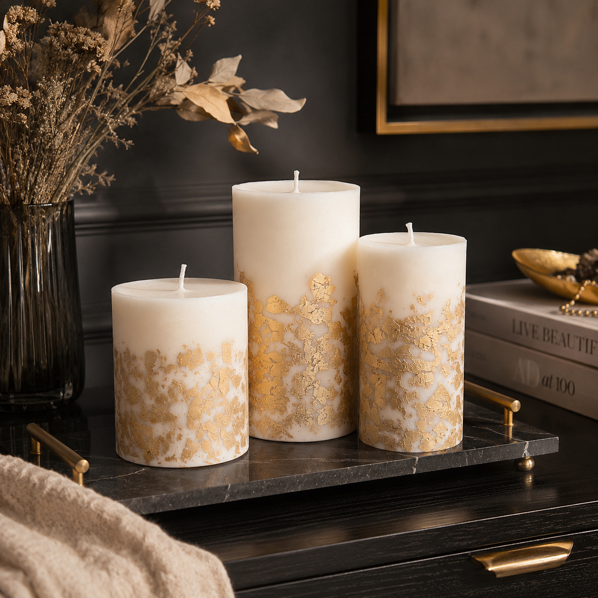 Handmade ivory pillar candles with metallic gold decoration displayed in an elegant dark interior