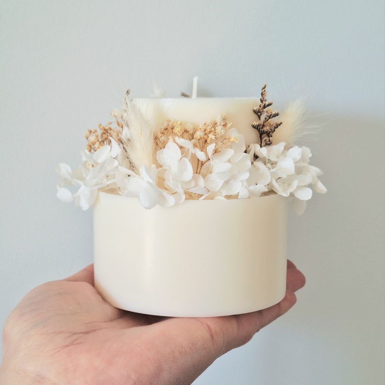 Ivory white botanical candle shown in hand for size reference