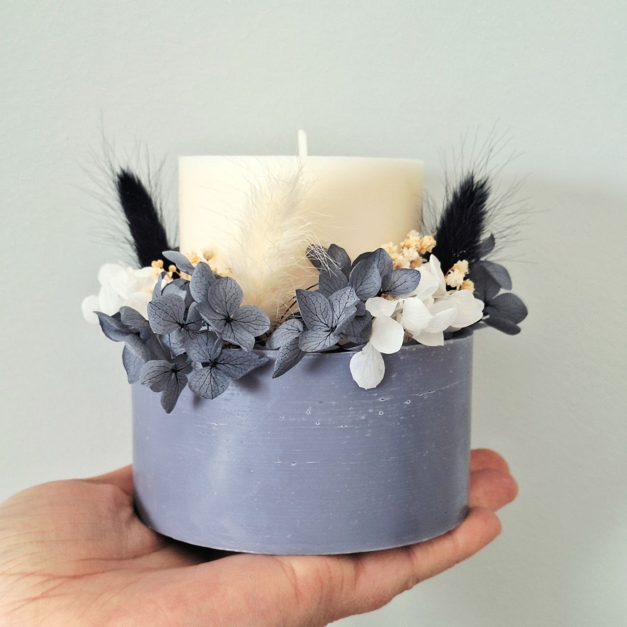 Midnight grey botanical candle shown in hand for size reference