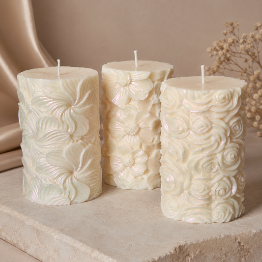 Pearlescent sculptural soy pillar candle with raised floral patterns displayed on a warm stone pedestal.