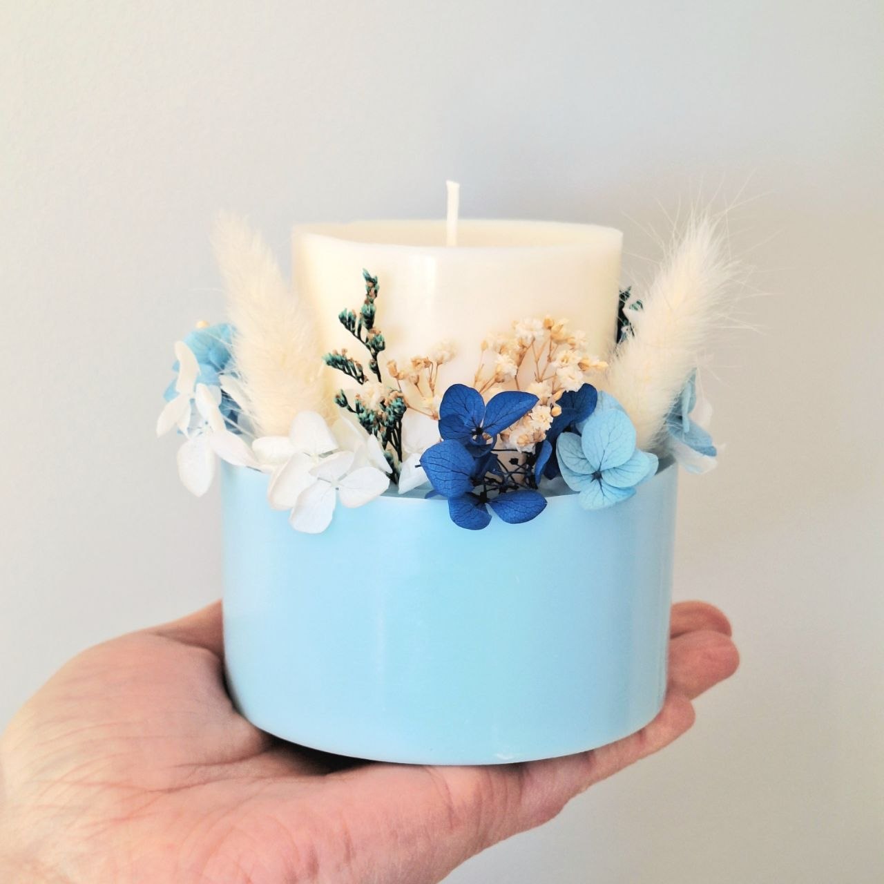 Powder blue botanical candle shown in hand for size reference