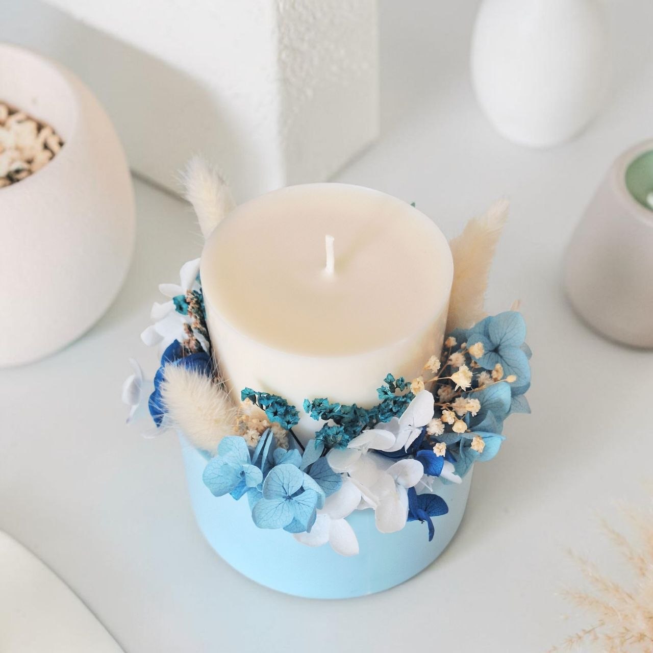 Top view of powder blue botanical candle with preserved blue and white flowers arranged around the candle