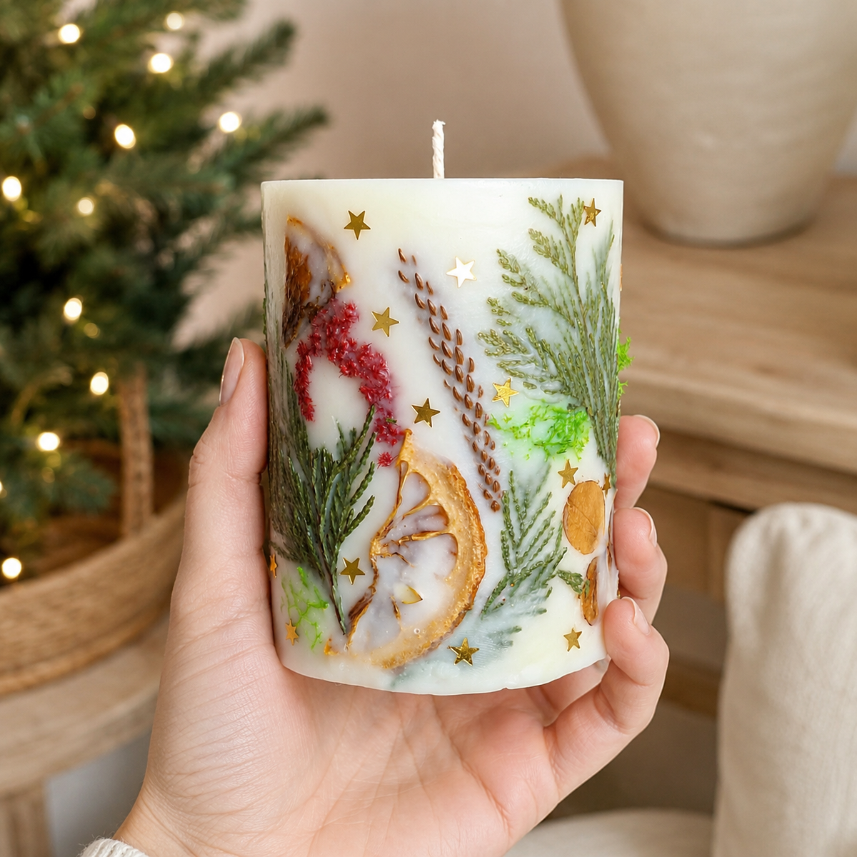Small botanical Christmas candle held in one hand to show its size and detailed natural decoration.